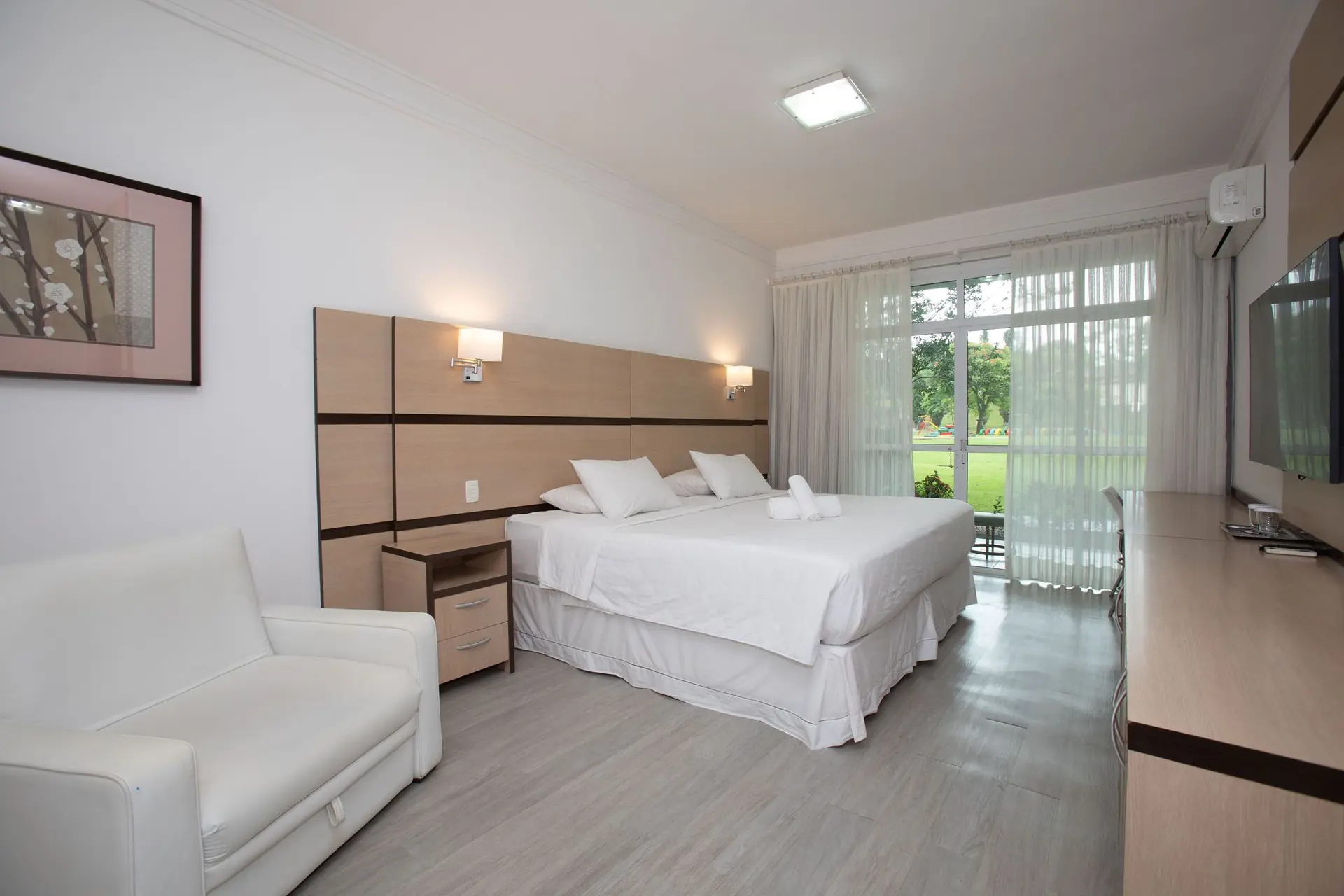 Quarto do Apartamento Máster do Spa Med, com cama de casal, poltrona e porta de vidro para o gramado