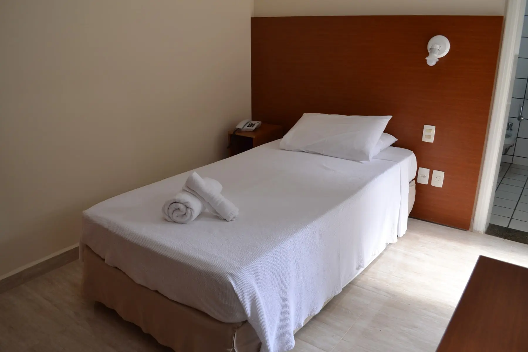 Quarto com cama de solteiro, cabeceira de madeira e toalhas dobradas sobre a cama