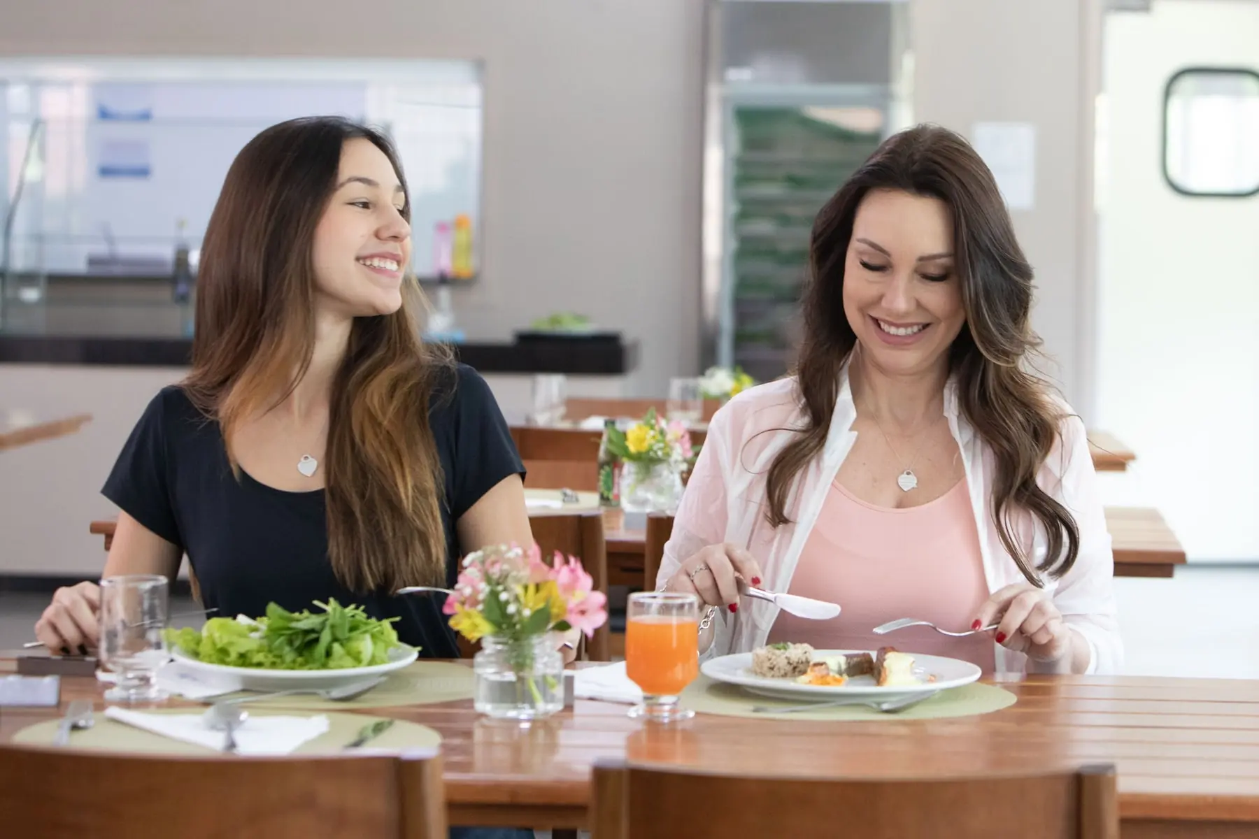 Duas hóspedes almoçando à mesa do restaurante, com salada e suco