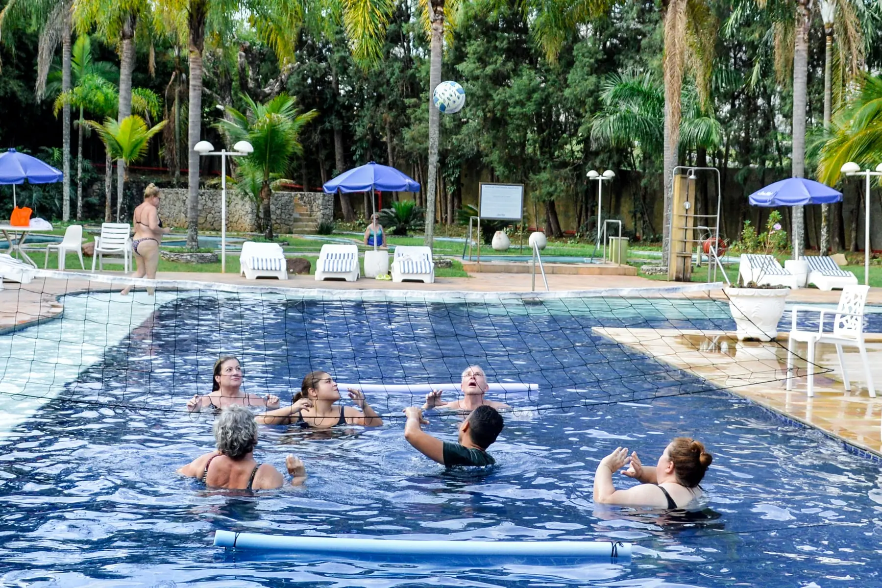 Hóspedes jogando bola na piscina externa do Spa Med, entre as palmeiras