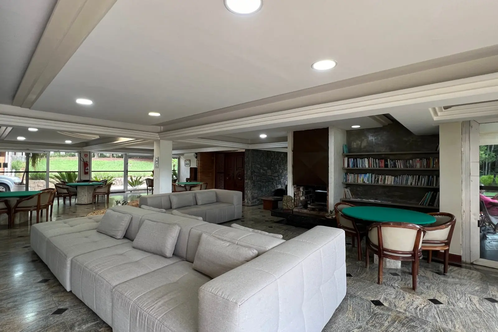 Salão da casa sede com sofás, estante de livros e mesa de carteado