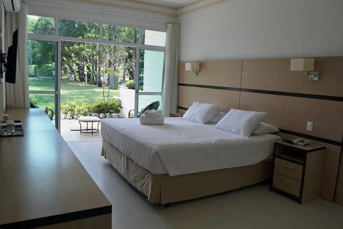 Apartamento Master com cama de casal e parede de vidro aberta para o jardim