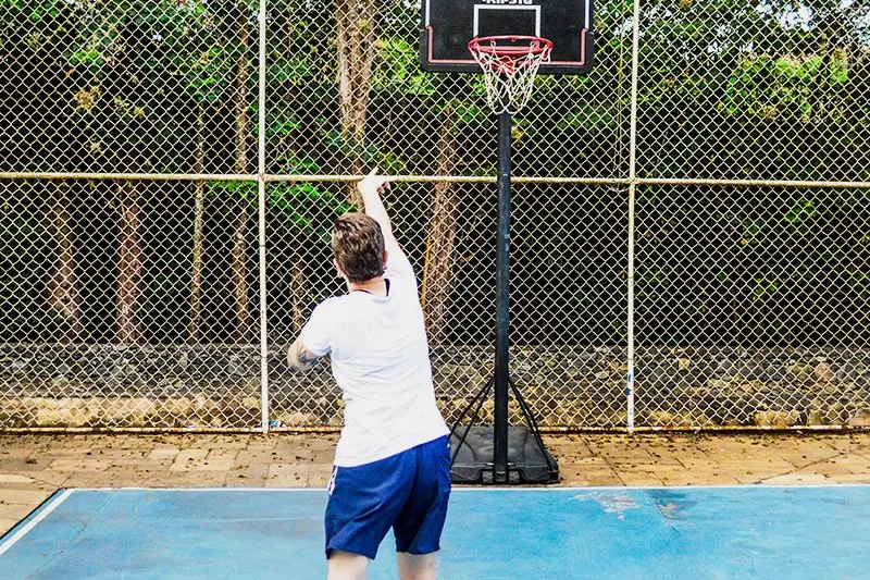 Hóspede arremessando ao cesto na quadra de basquete, cercada por alambrado e árvores