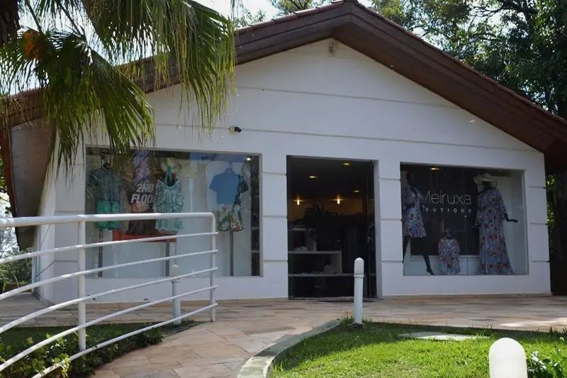 Fachada envidraçada da boutique, com o gramado e o caminho de pedra à frente