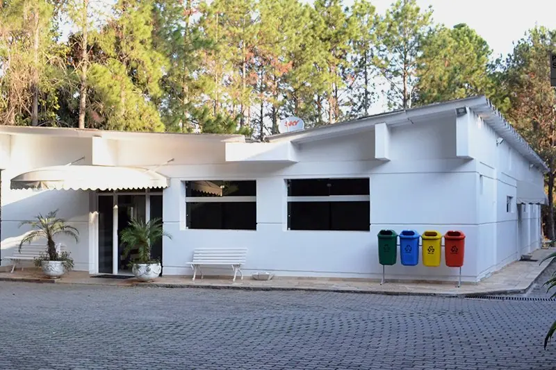 Bloco branco do centro médico visto da via de acesso, com pátio de pedra portuguesa à frente