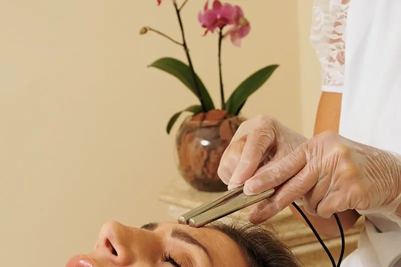 Tratamento facial em andamento, com a hóspede deitada e a profissional conduzindo o aparelho