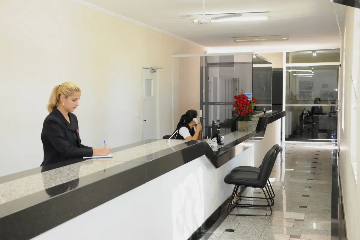 Balcão de atendimento do concierge, em granito preto, com atendente e área de trabalho ao fundo