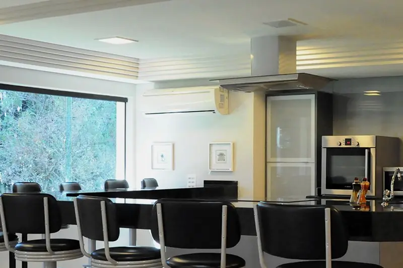 Bancada da cozinha experimental com banquetas altas e piso xadrez, aberta para o jardim