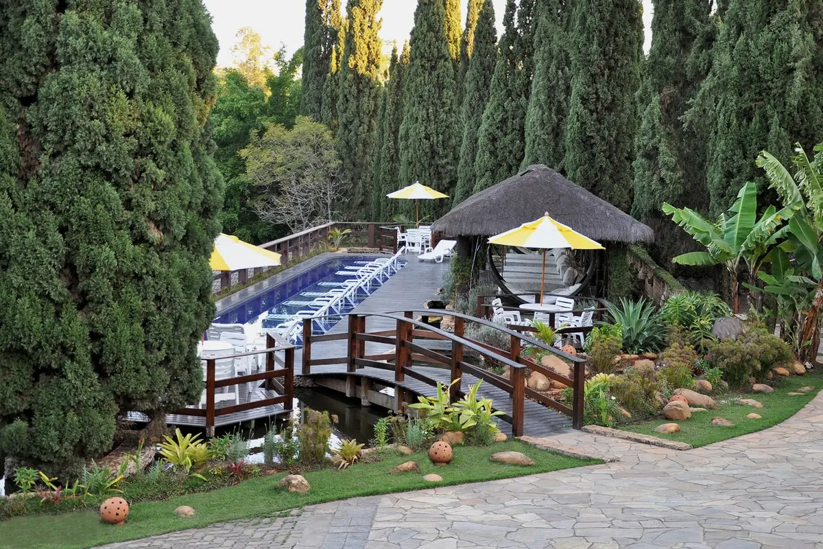 Piscina vista de cima com ponte de madeira, quiosques de palha e guarda-sóis amarelos