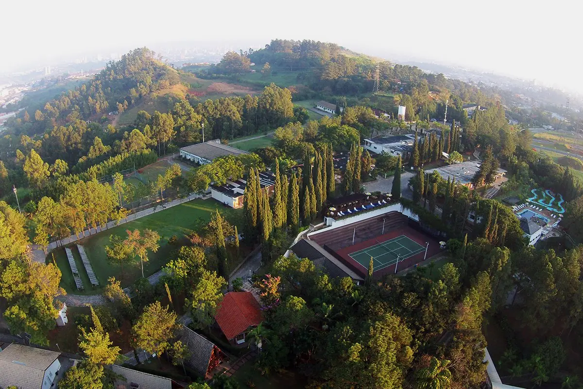 Vista aérea do Spa Med, com os blocos baixos espalhados entre a mata, a quadra de tênis e as piscinas