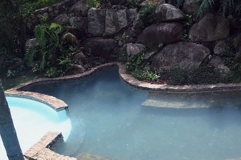 Piscina de borda de pedra natural cercada de rocha e vegetação, com cascata ao fundo