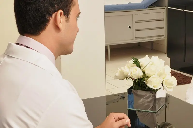 Médico sentado à mesa do consultório, anotando, com vaso de flores brancas ao lado