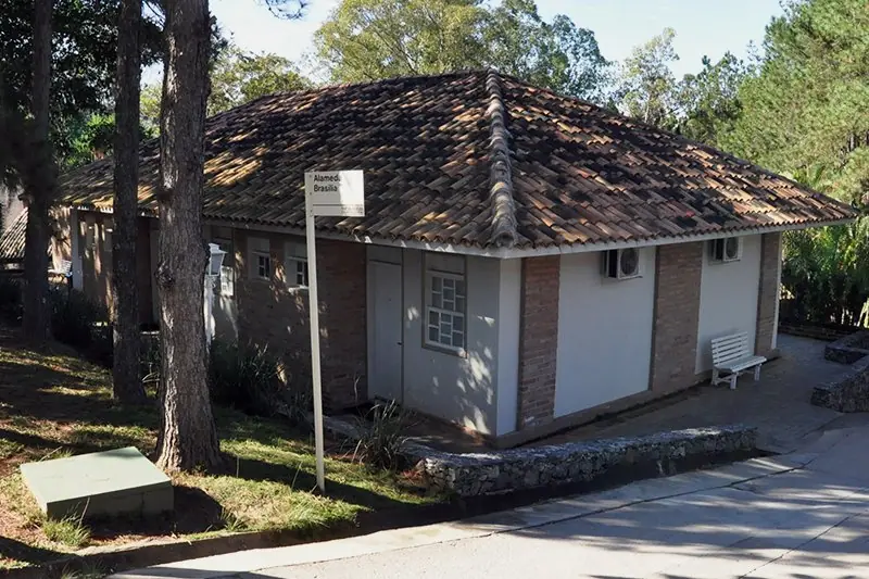Bloco Colonial Mineira de telhado de telha e alvenaria clara, entre pinheiros