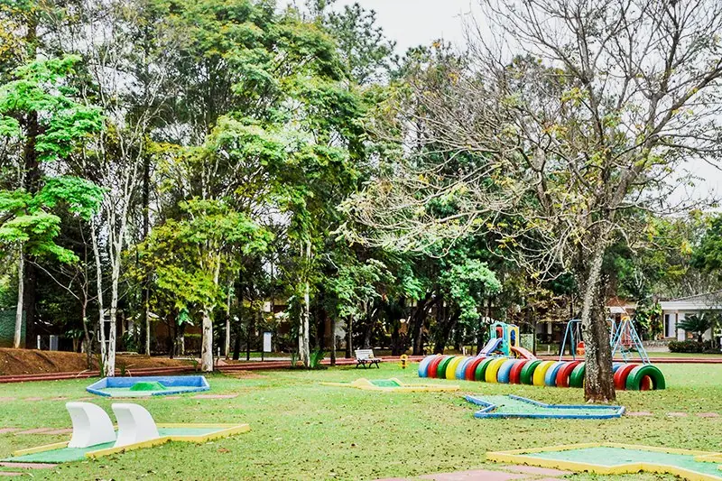 Percurso de mini golfe no gramado, com obstáculos coloridos entre as árvores