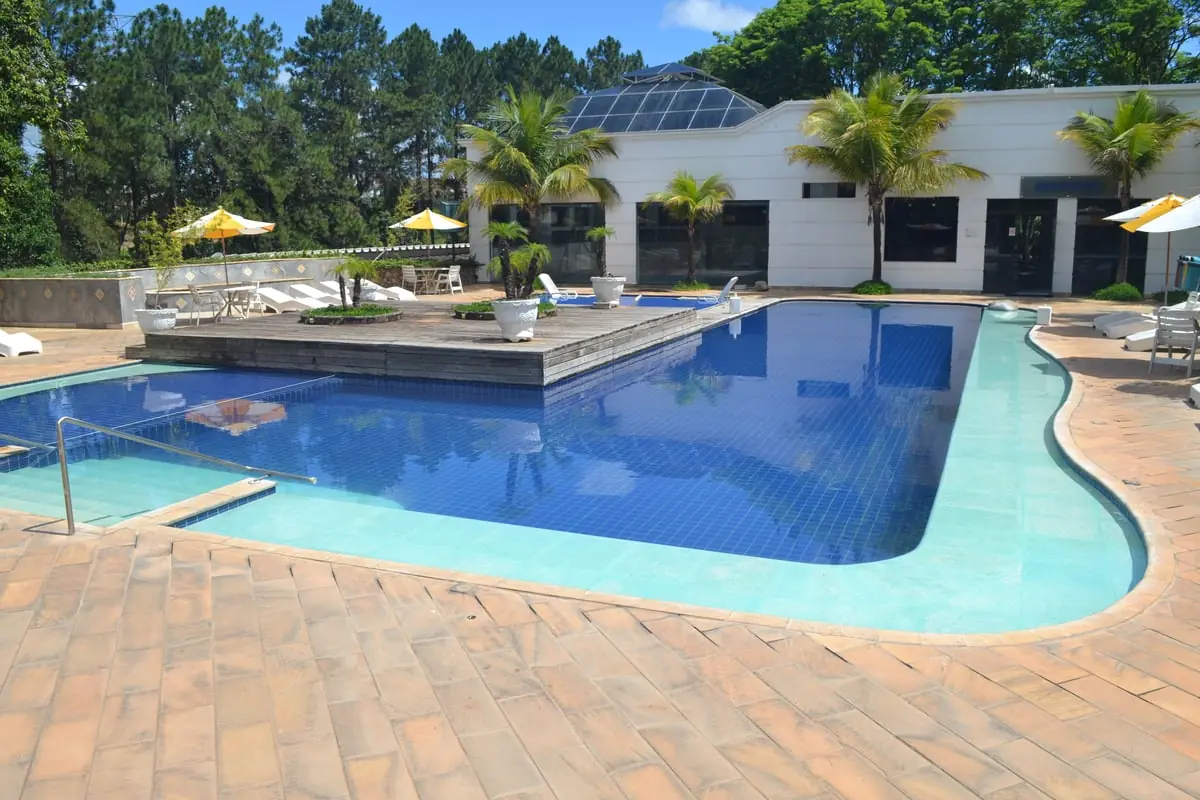 Piscina de borda azul em frente ao bloco de acomodações, com guarda-sóis amarelos
