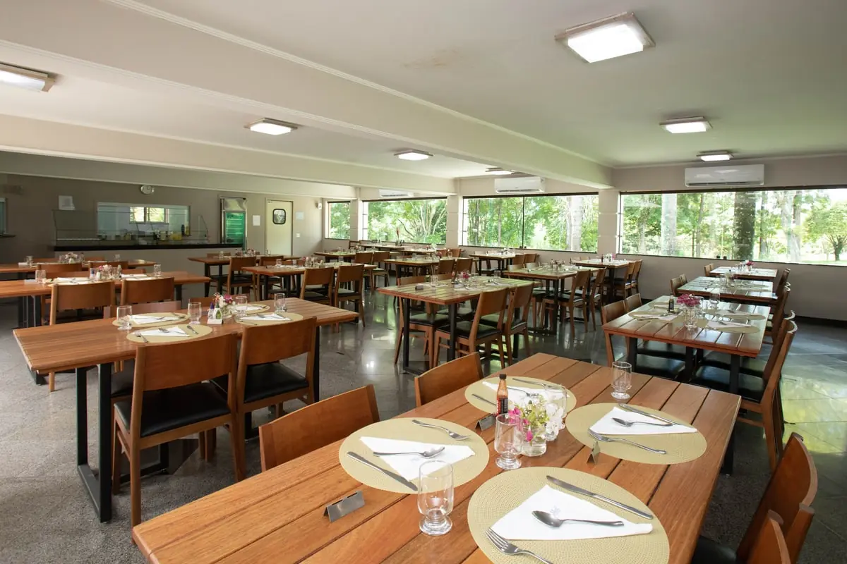 Salão do restaurante com as mesas postas e as janelas para o verde