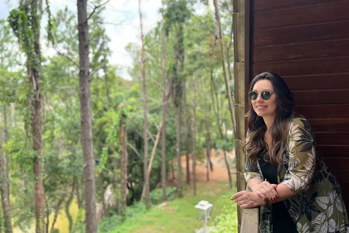 Hóspede na varanda de madeira do chalé, de frente para os pinheiros