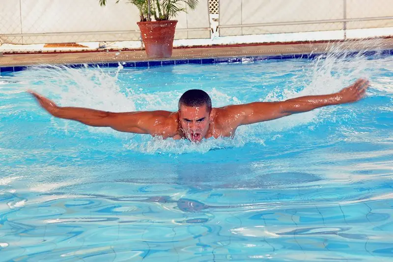 Nadador executando a braçada de borboleta na piscina, com a água espirrando