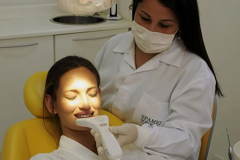 Atendimento odontológico em cadeira clínica, com a dentista de máscara trabalhando sob o refletor
