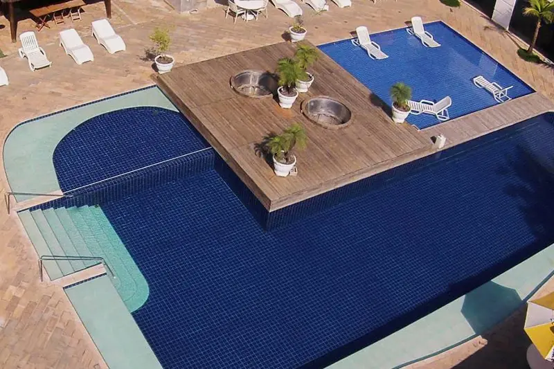 Deck de madeira avançando sobre a piscina azul, com espreguiçadeiras e vasos