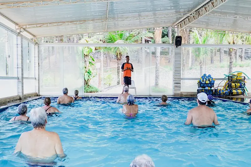 Grupo de hóspedes em aula dentro da piscina coberta, com o professor de pé na borda