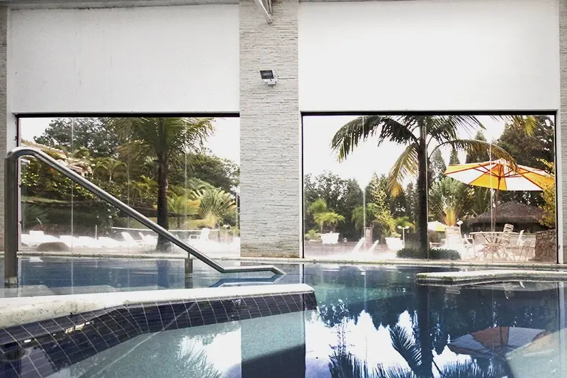 Piscina interna de borda arredondada, com vista para o deck externo pela parede de vidro