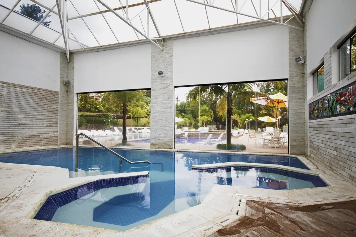 Piscina interna aquecida sob telhado translúcido, com a área externa ao fundo