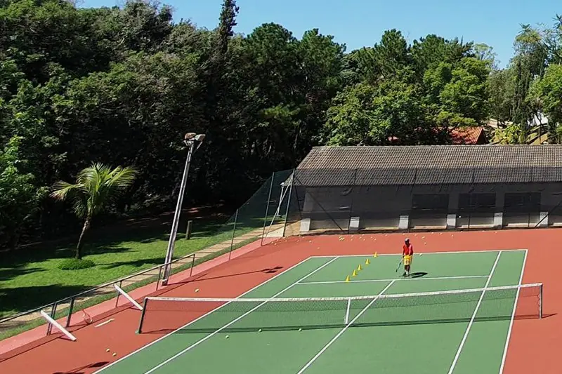 Quadra de tênis de piso verde e vermelho, com dois jogadores e a mata em volta
