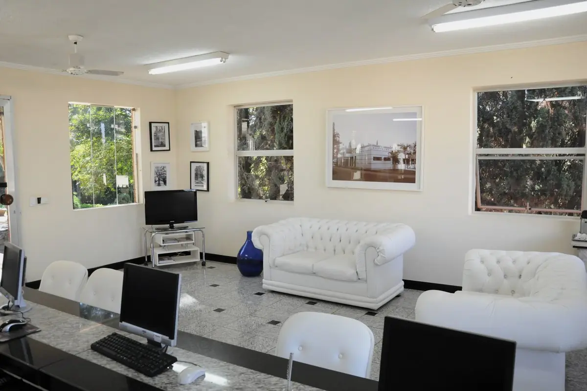 Sala de estar com sofás brancos capitonê, computador de consulta e quadros na parede