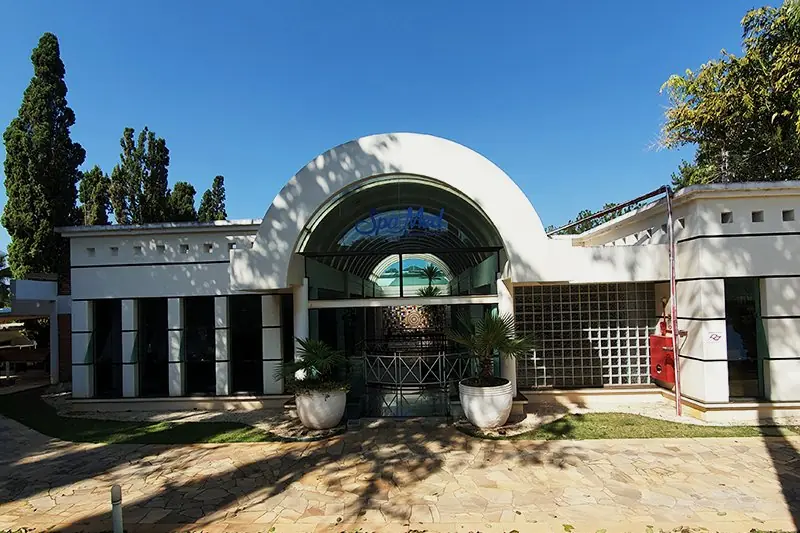 Bloco do restaurante com marquise curva de concreto e vidro, visto do gramado