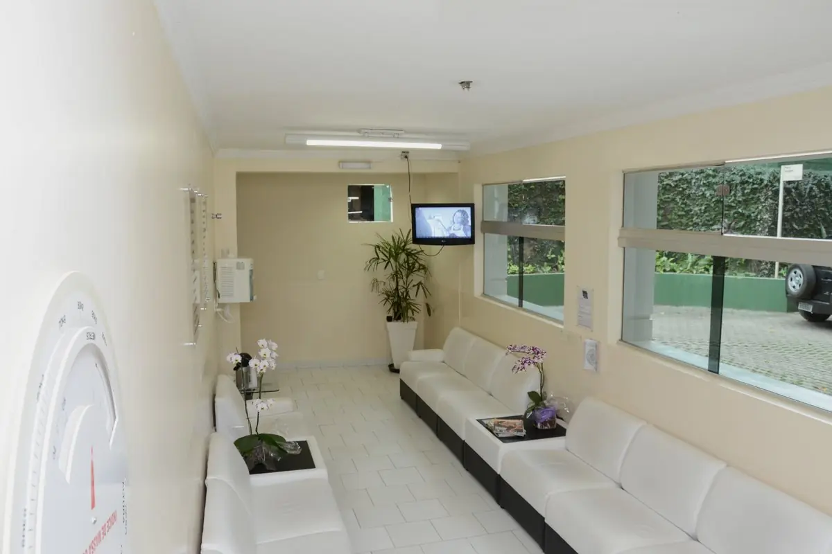 Sala de espera com sofás brancos, orquídeas sobre a mesa baixa e janelas para o jardim