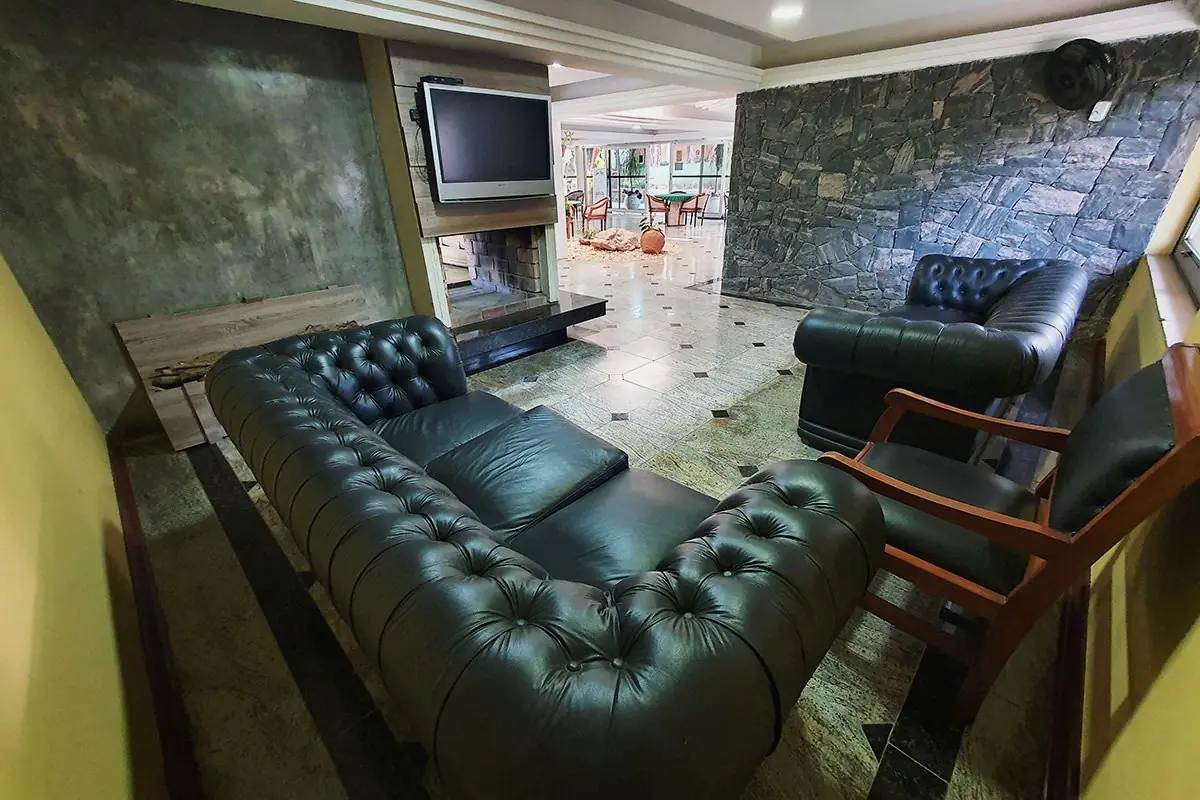 Sala de estar com sofás de couro verde e televisão, junto à parede de pedra