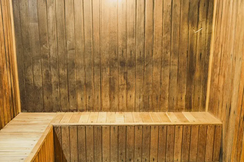 Interior da sauna seca, toda em madeira clara, com banco corrido de dois níveis