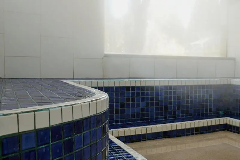 Interior da sauna úmida, com banco curvo de azulejo azul e luz difusa pela claraboia