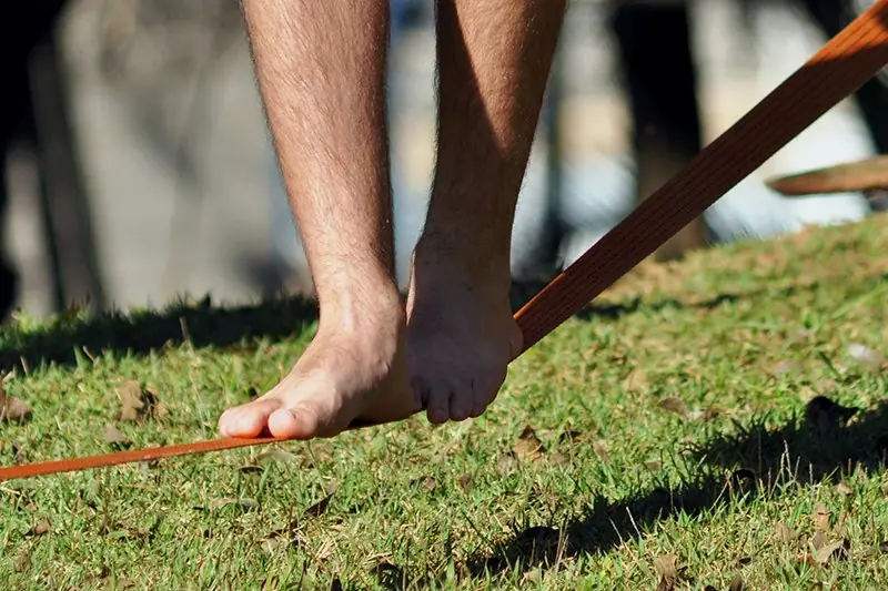Praticante equilibrando-se na fita de slackline esticada sobre o gramado