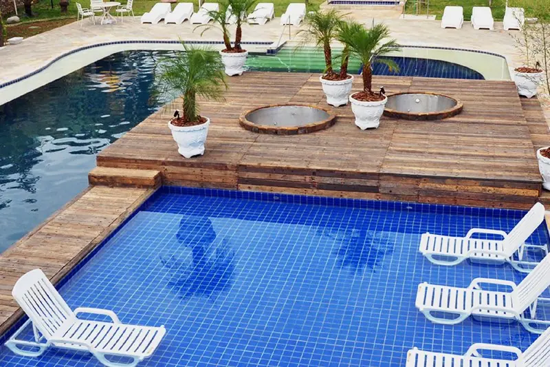 Deck de madeira com espreguiçadeiras brancas entre dois trechos de piscina azul