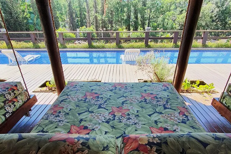 Cama de descanso estofada sob o quiosque de madeira, voltada para a piscina