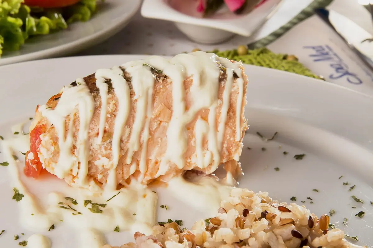 Prato montado com peixe grelhado, risoto de grãos e legumes, servido em louça branca
