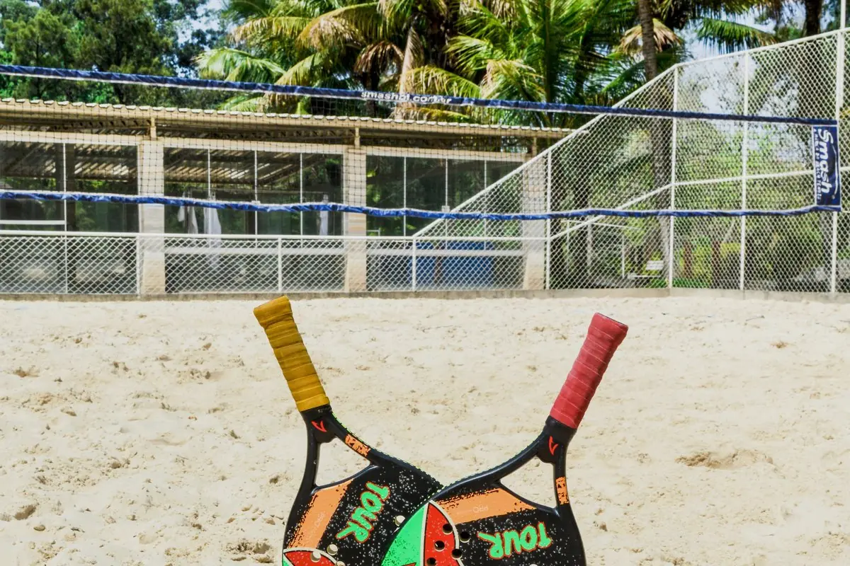 Duas raquetes de beach tennis e bolinhas sobre a areia da quadra