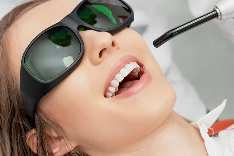 Aplicação de laser odontológico, com a paciente de óculos de proteção na cadeira
