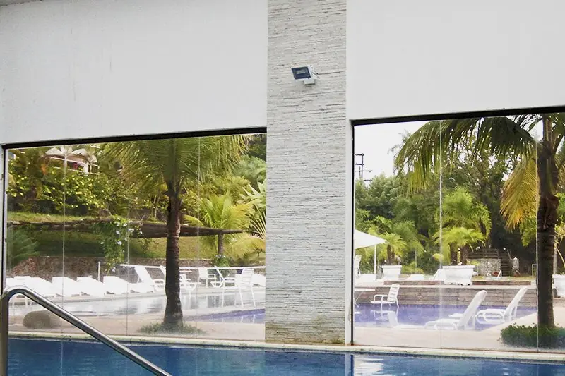 Piscina interna aquecida sob a cobertura de vidro, com espreguiçadeiras e o verde do lado de fora