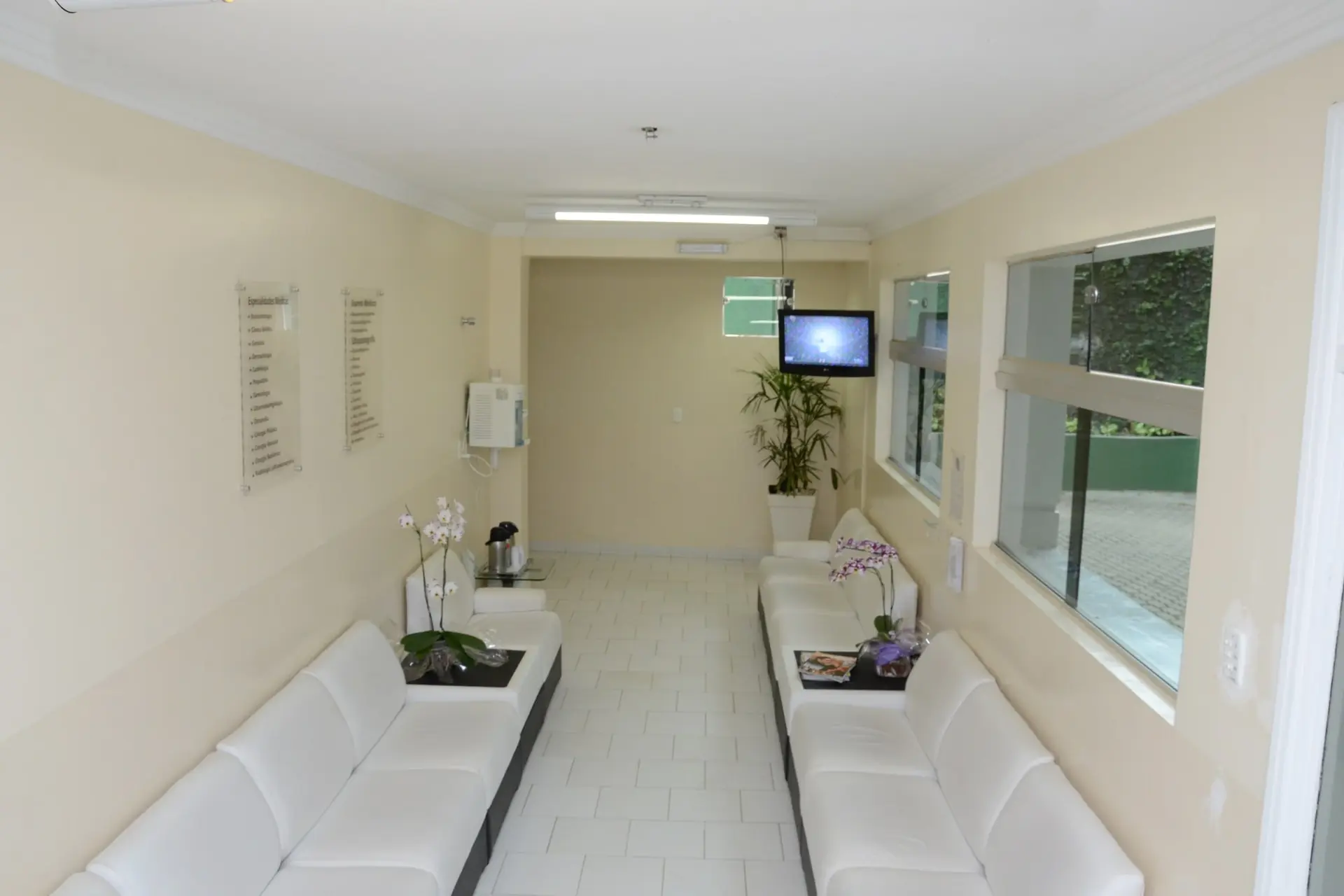 Sala de espera do centro médico do Spa Med, com sofás brancos, orquídeas e janelas para o jardim