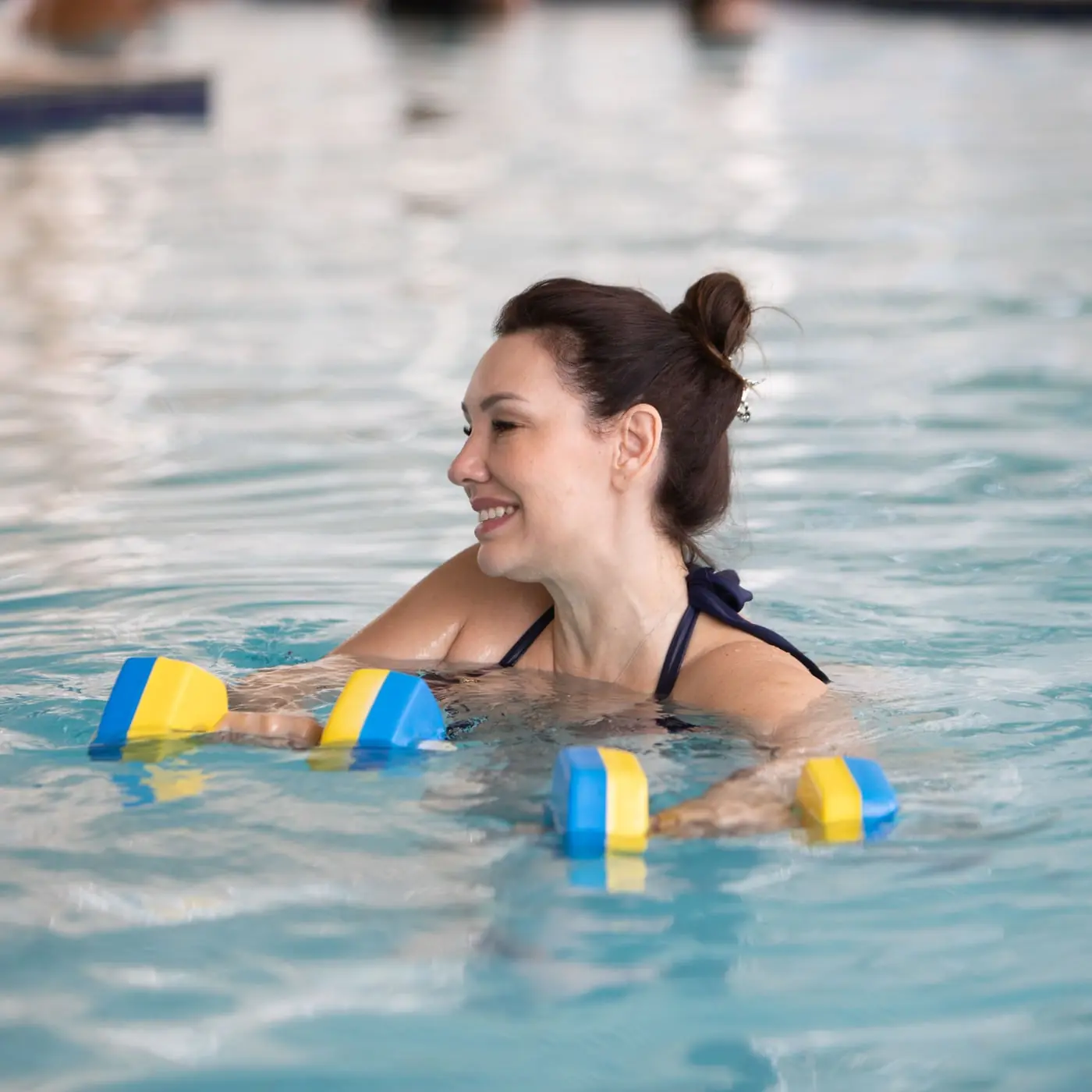 Hóspede em aula de hidroginástica com halteres de espuma na piscina coberta