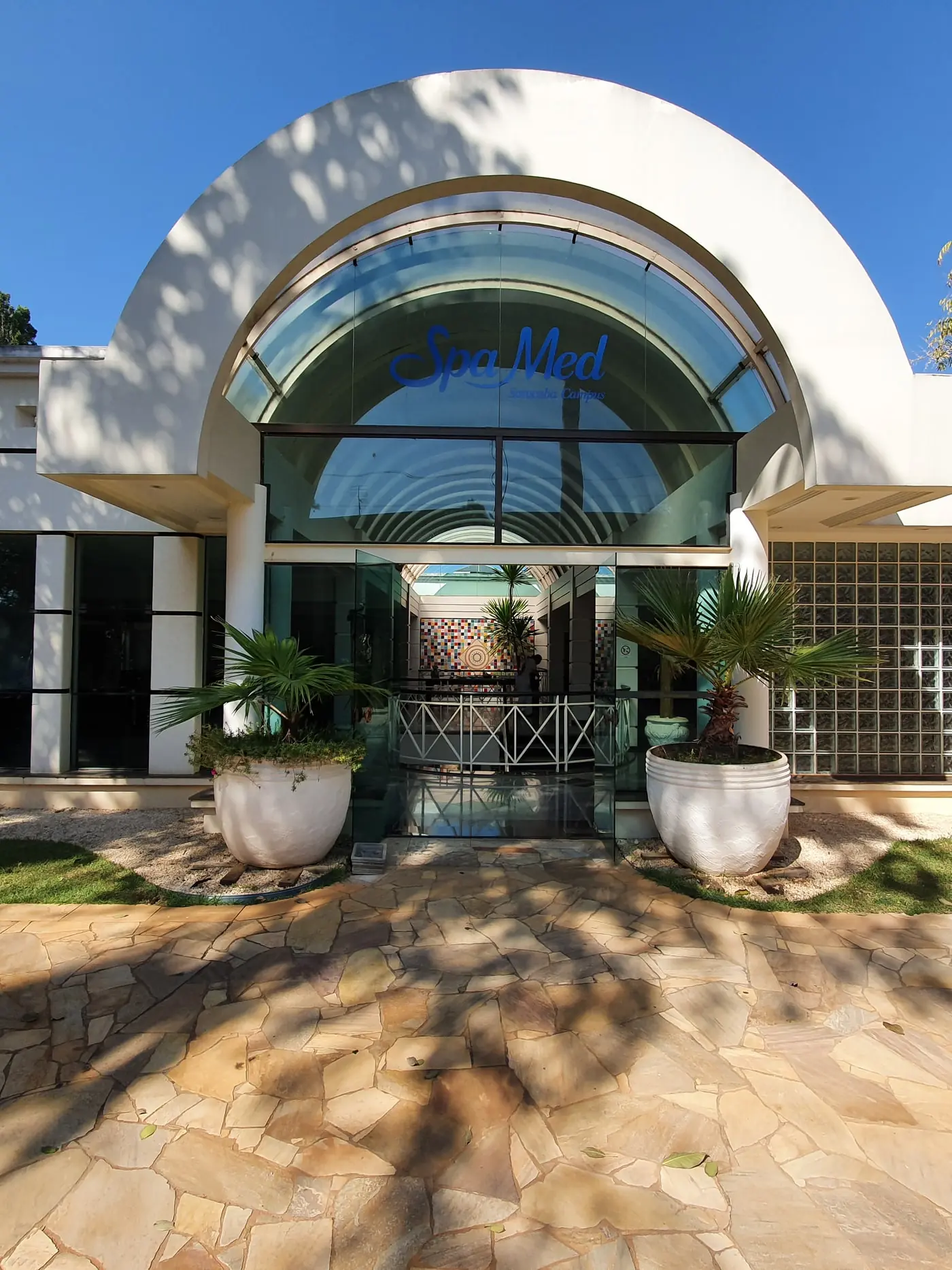 Fachada da recepção do Spa Med, com a entrada em arco de vidro e o caminho de pedra